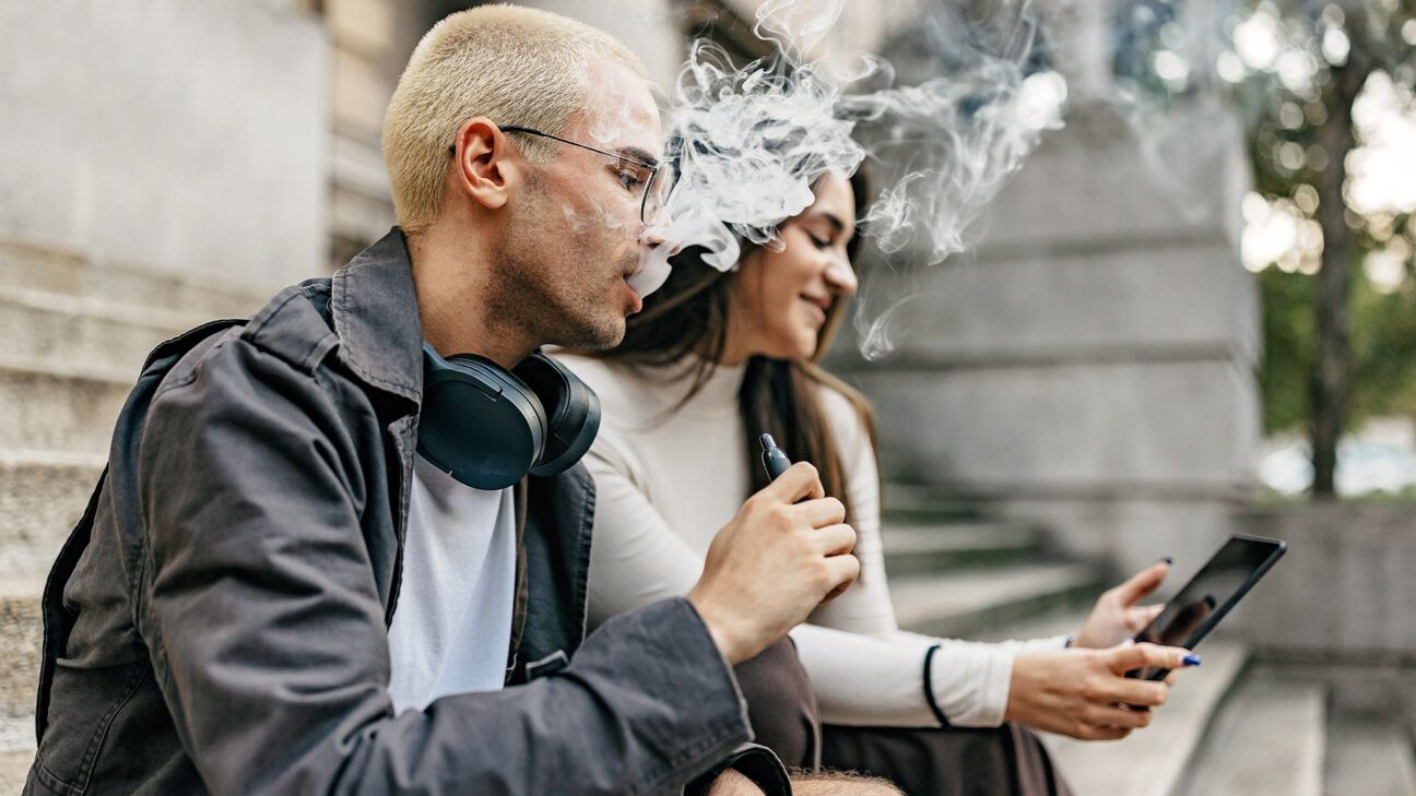 Male and female young adult vaping outside