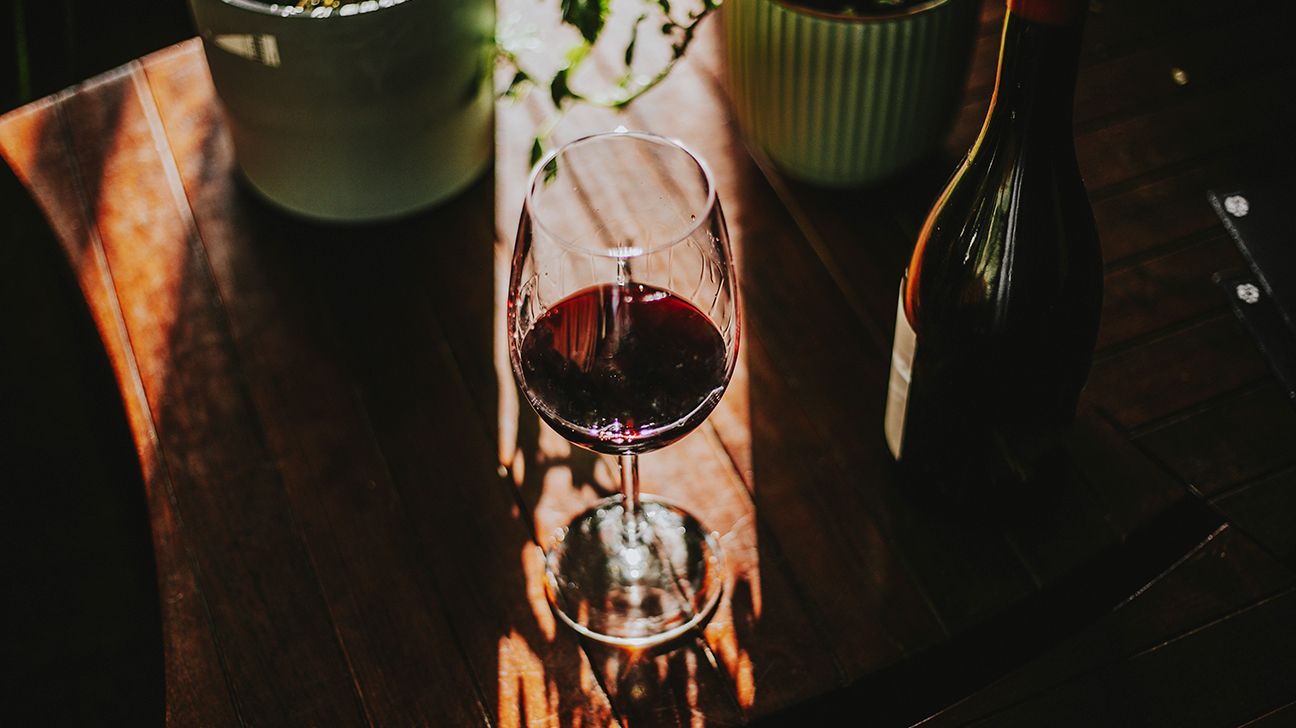 Sunlight streaming on glass of red wine on a table with potted plants in the background