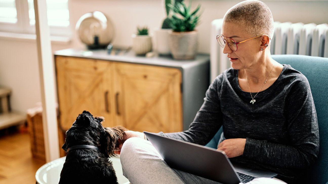 Older female sitting in an armchair with a laptop, petting a dog