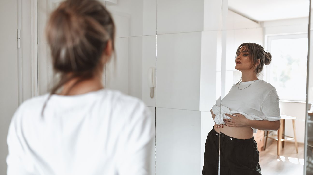 woman examining her body's reflection in the mirror
