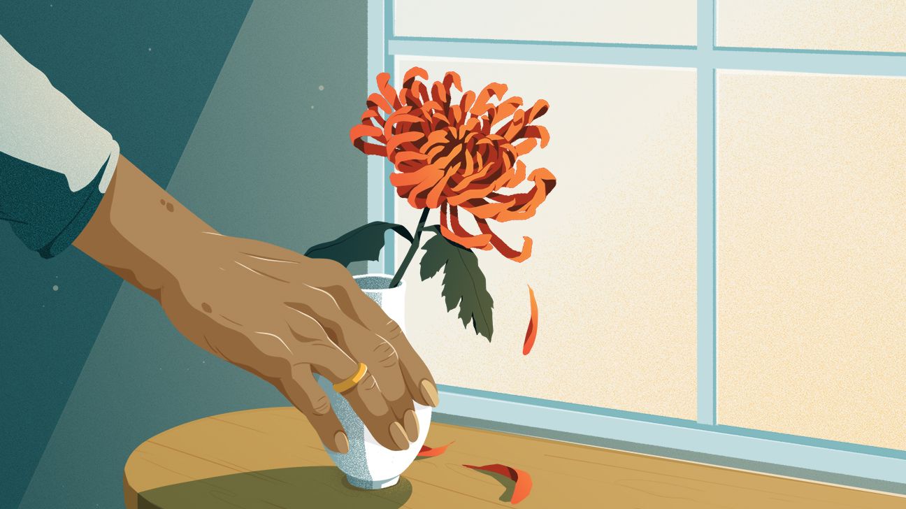 A woman places her hand on a flower in a window sill.
