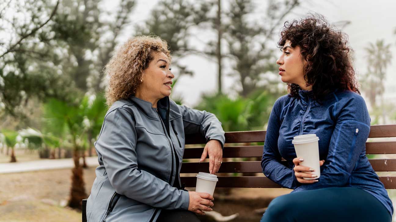 an older adult speaking to a younger adult on a park bench