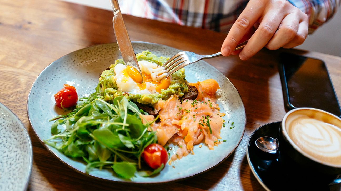 Hands cutting into avocado toast with egg and salmon salad
