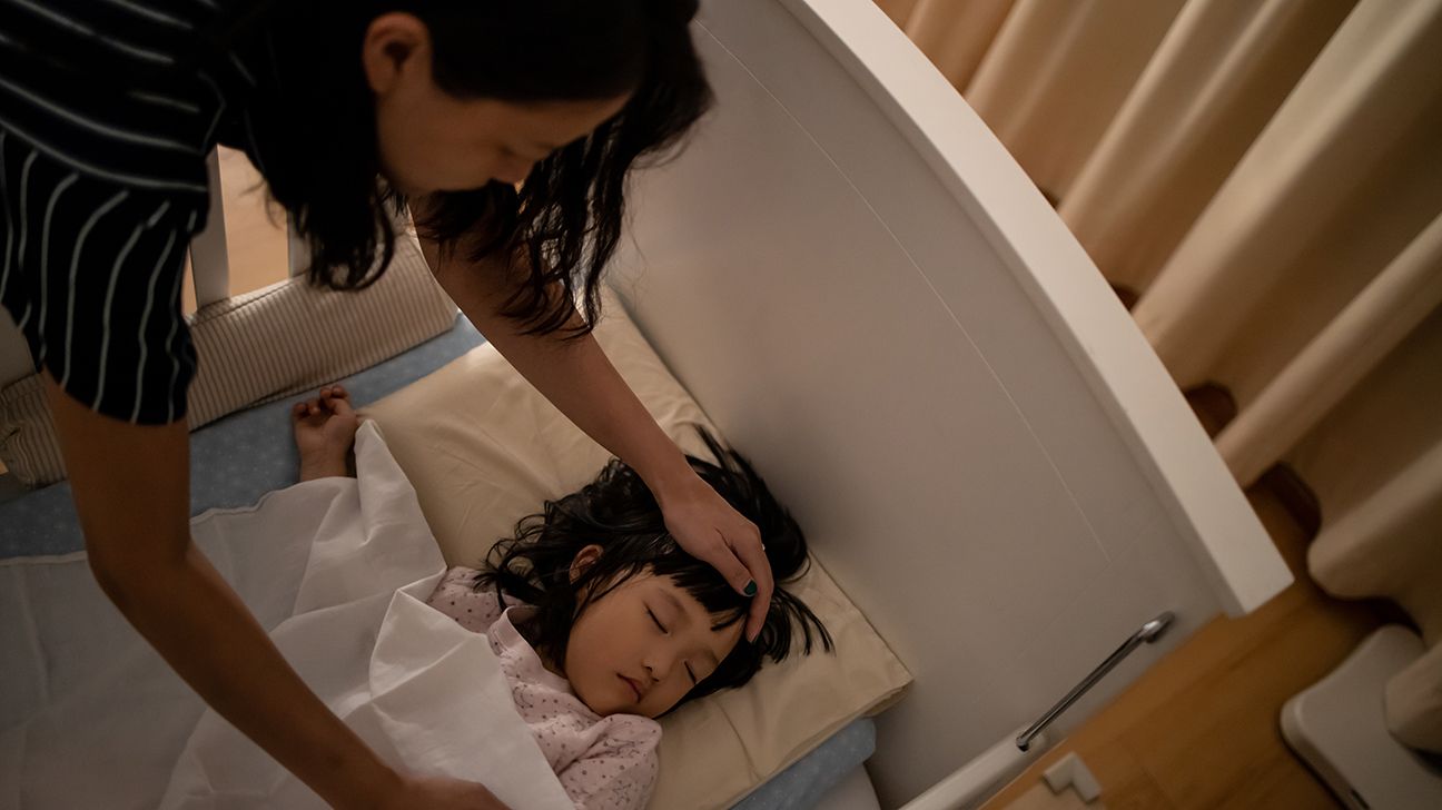 parent checking forehead of child who's lying in bed