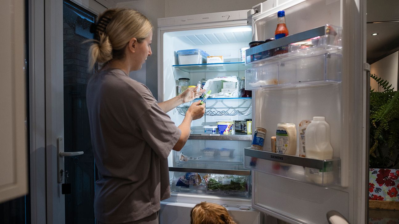 Woman removing injection pen from open refrigerator (or returning it)