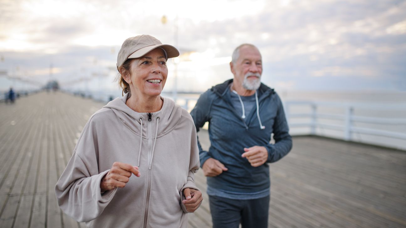 older adult couple running by the water