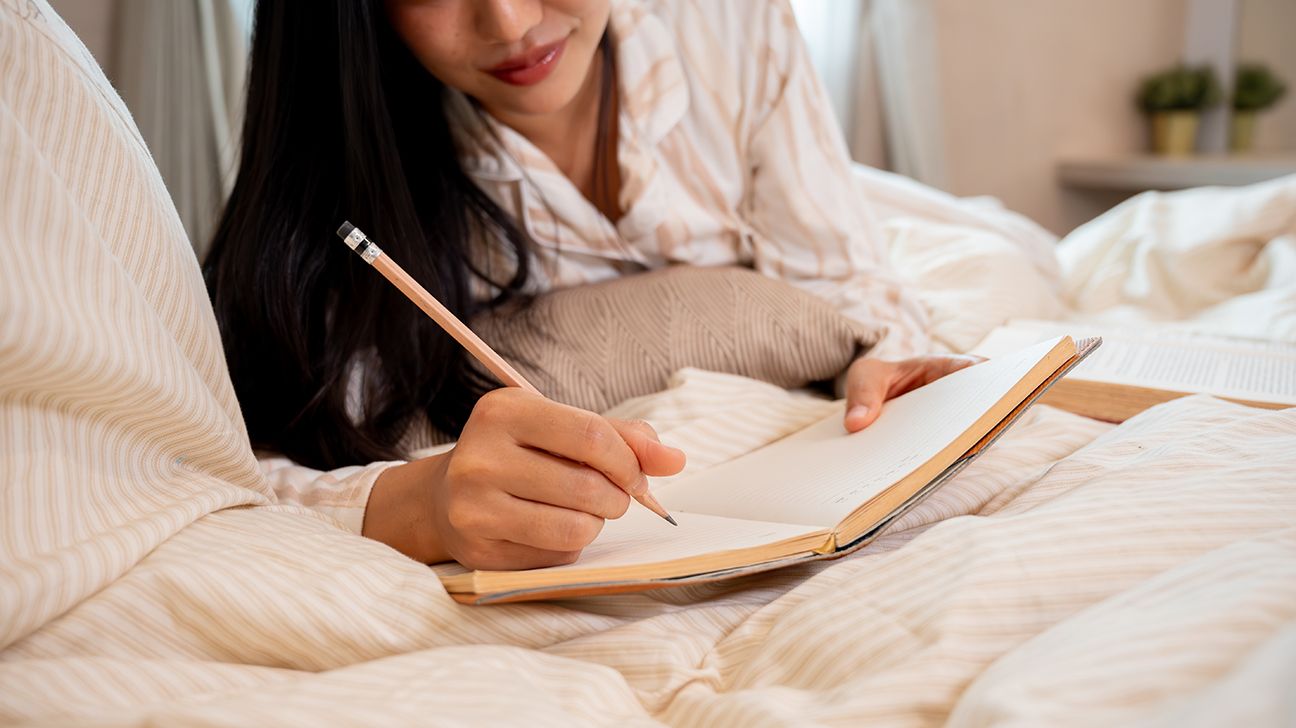 person writing in a journal in bed
