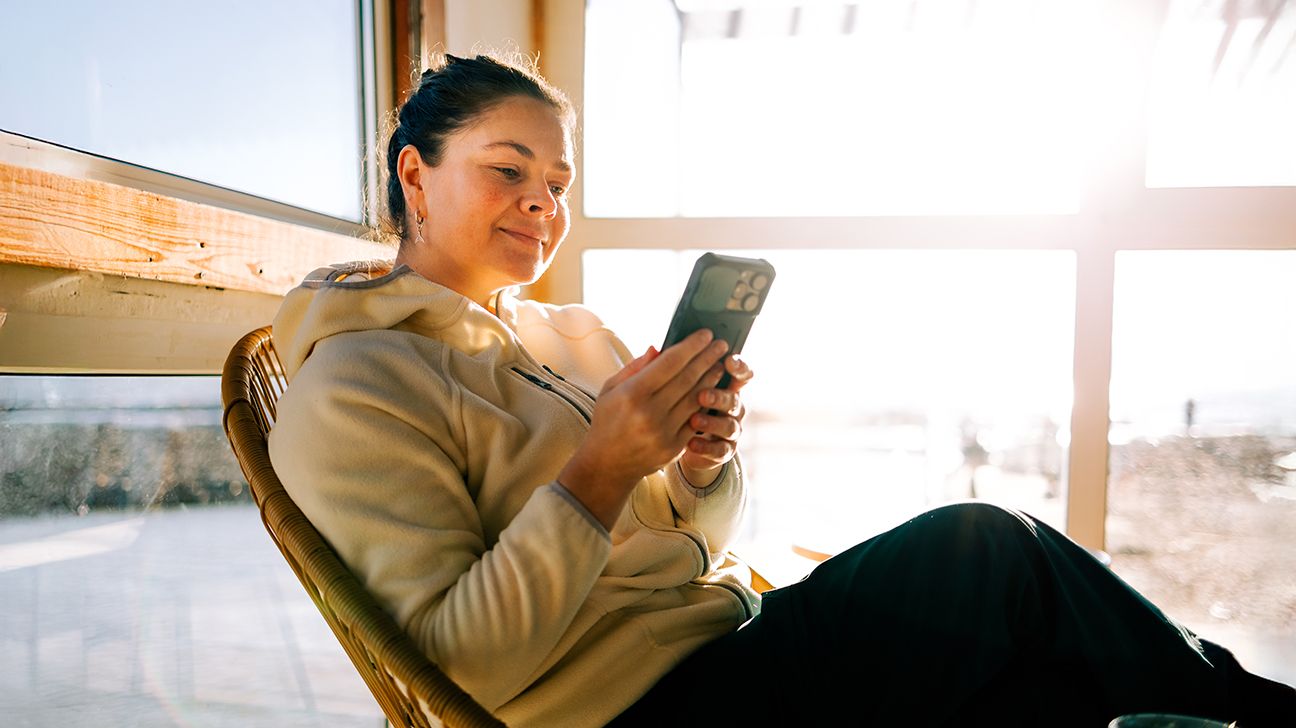 adult female using her phone in front of a window