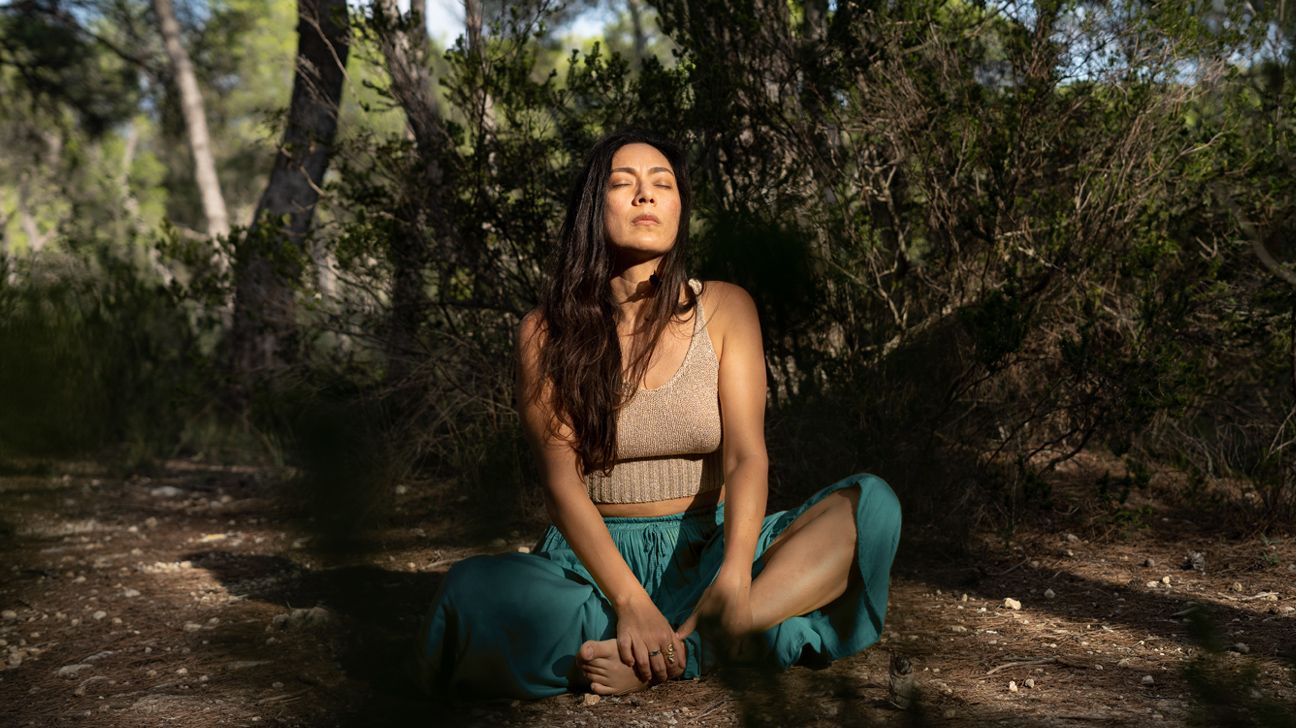 Woman sitting cross-legged in a forest with her eyes closed