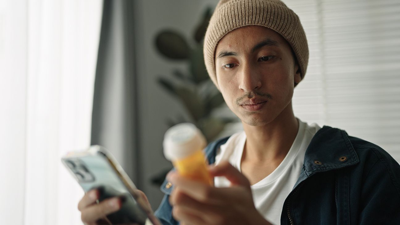 Man holding phone and looking at pill bottle