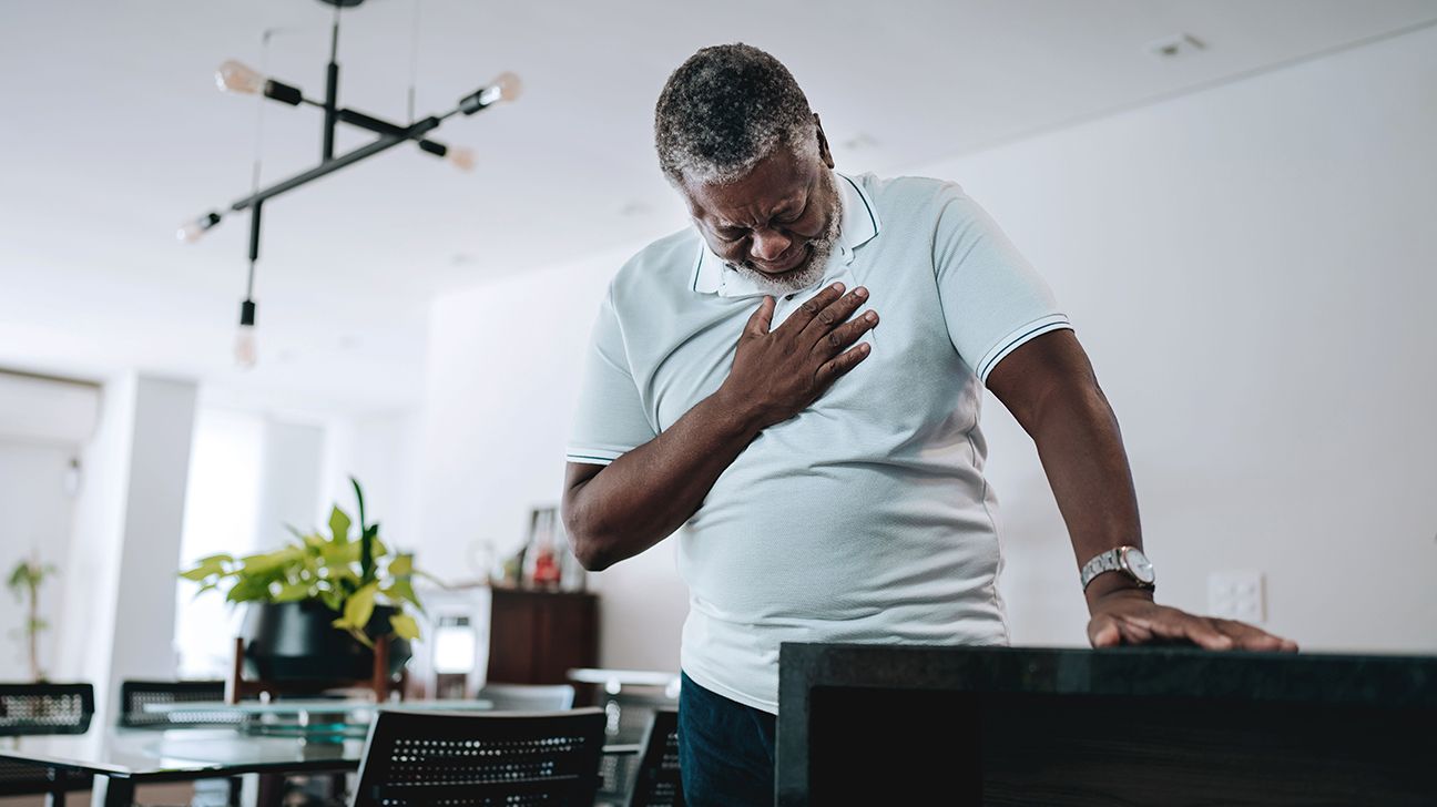 Dark-skinned senior man looking downward with one hand over his chest while standing