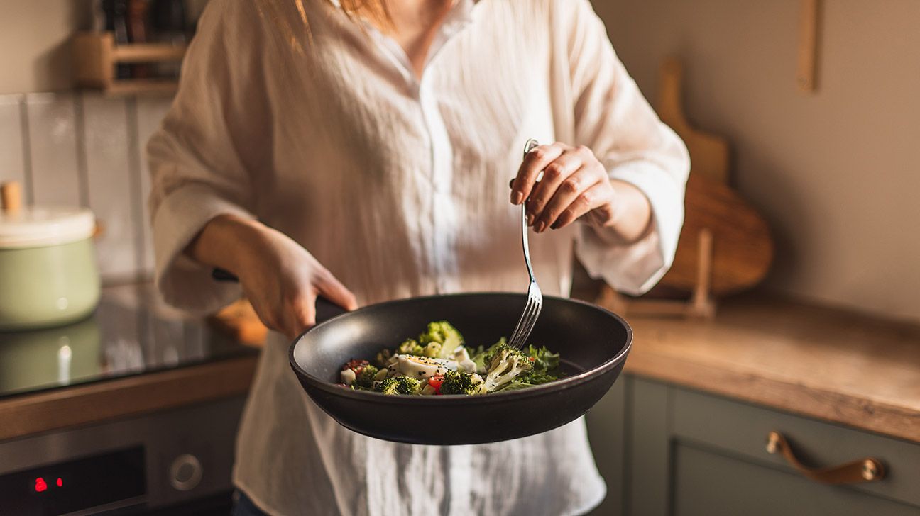 una mujer cocina vegetales en un sarten
