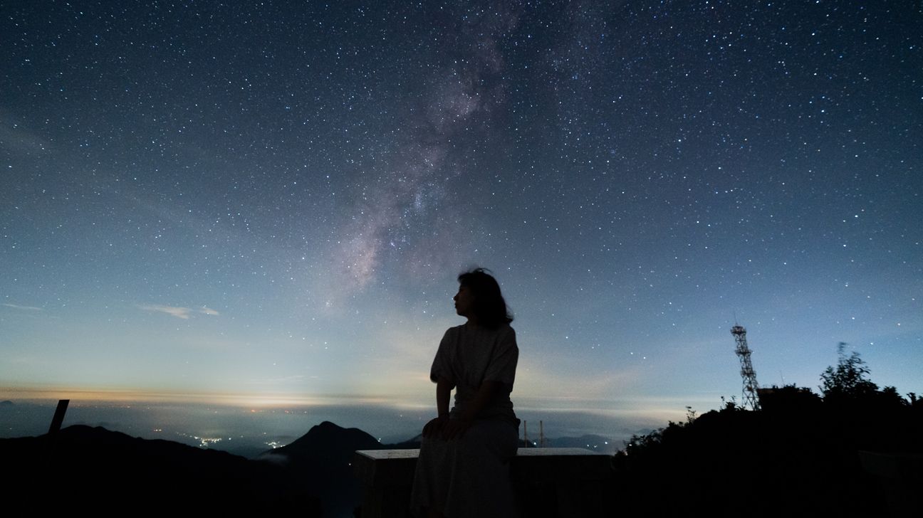 silhouette of a person sitting under the milky way at night