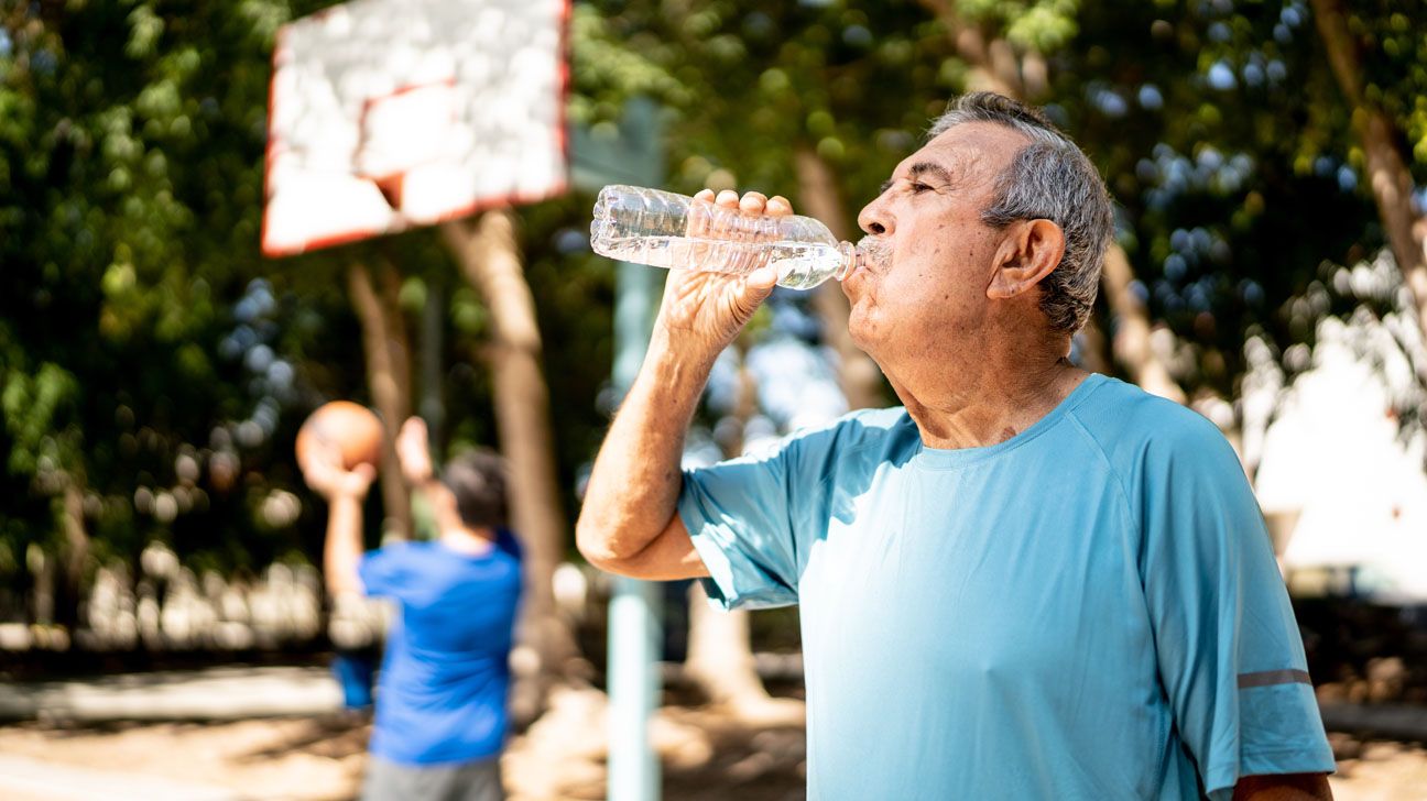 Older male drinking water outside in heat