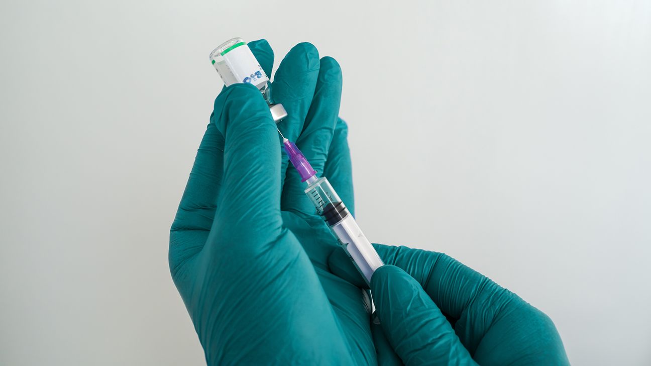 Close-up of hands in medical gloves drawing solution from a vial into a syringe