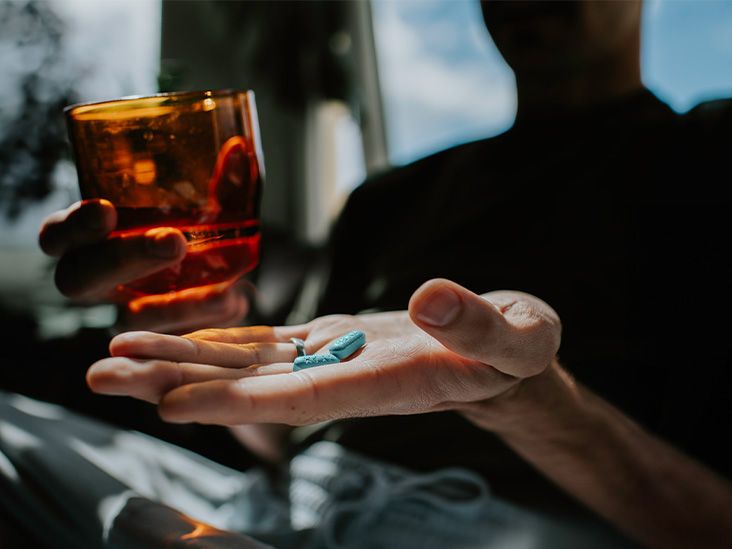 A person holds pills in one hand and a glass of water in another.