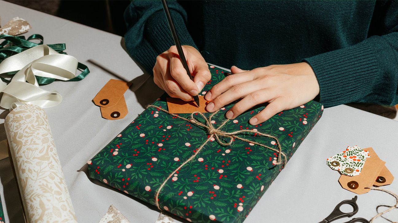 person writing on a gift tag, ready to place on a freshly wrapped present
