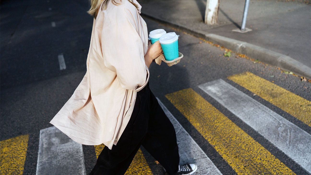 Female carrying paper to-go coffee cups while crossing the road