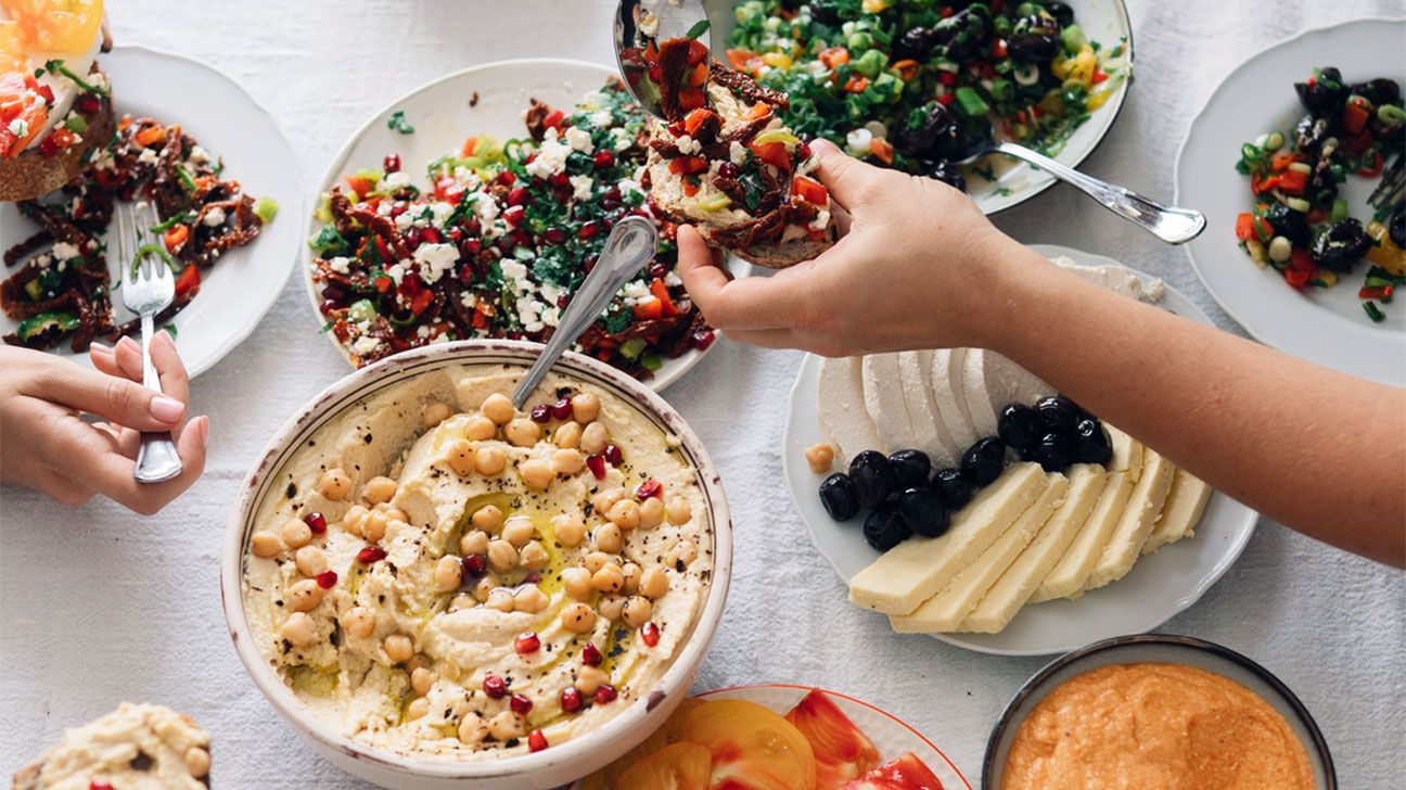 People sharing food at a table, including hummus and vegetables