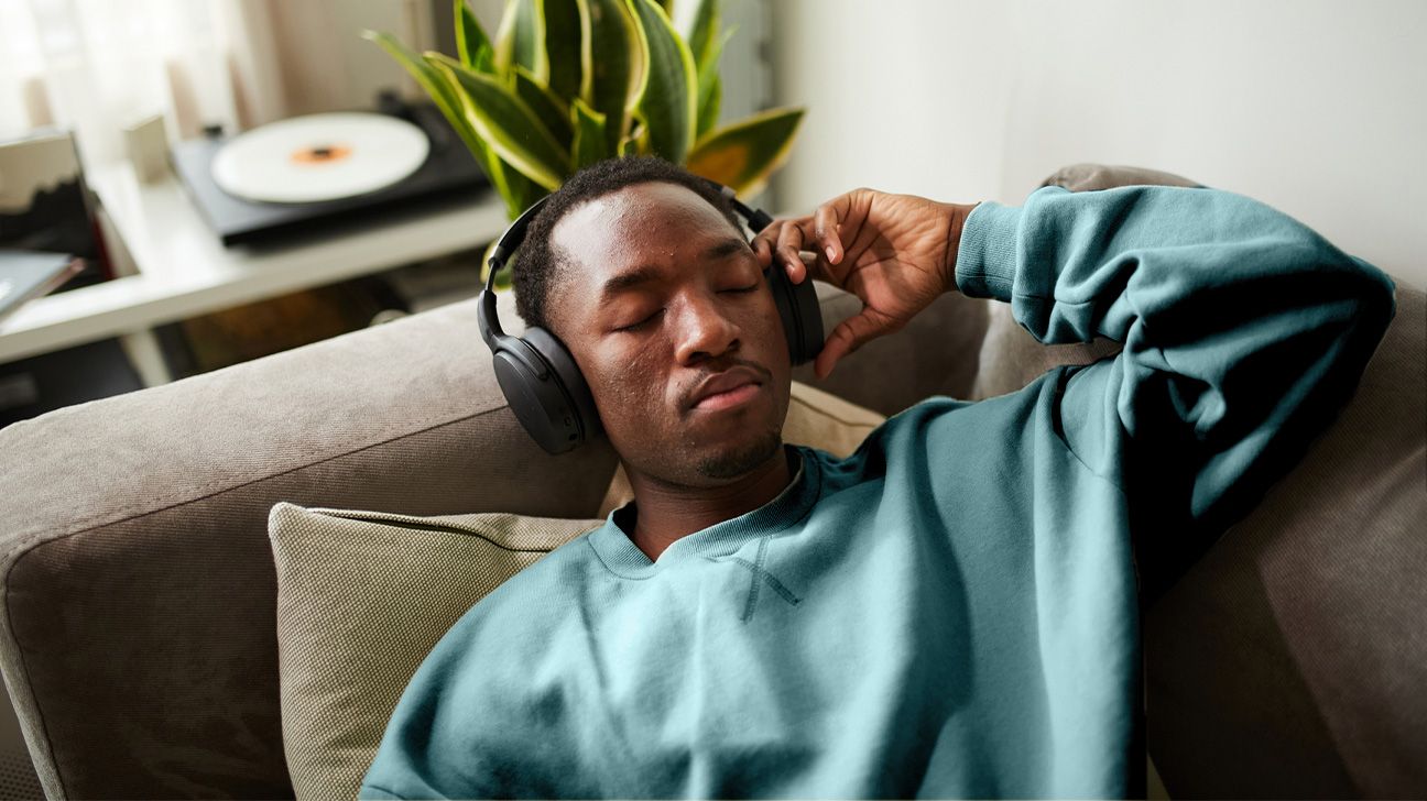 Male lying on a sofa with headphones on and his eyes closed