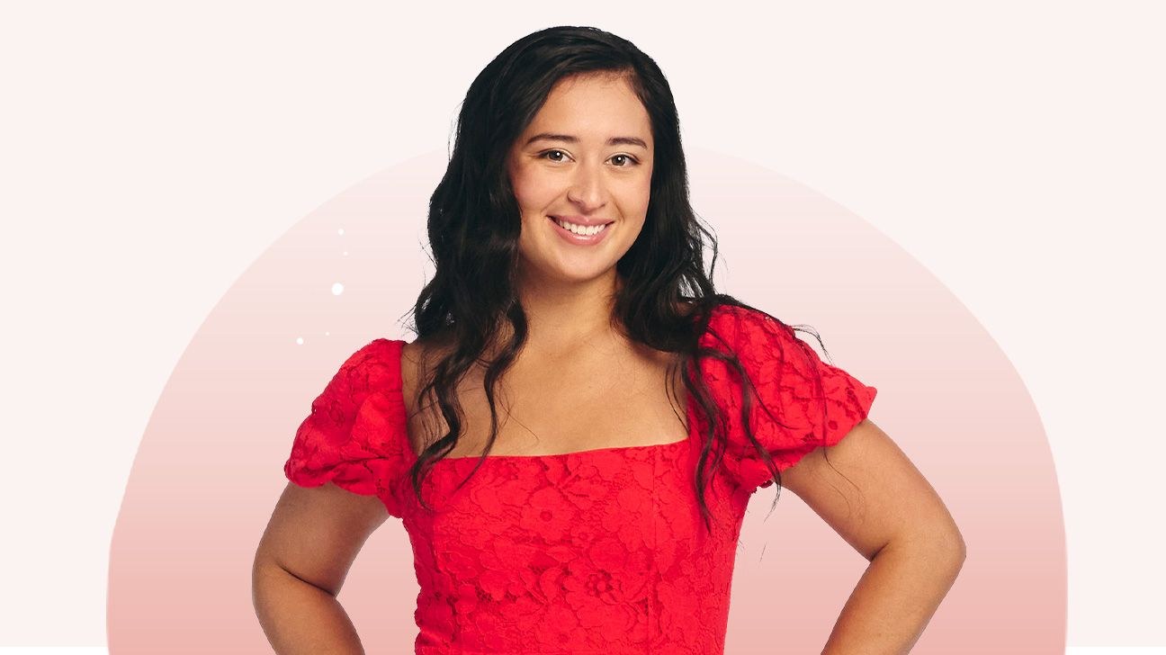 Alex is wearing a red dress and smiling with her hands on her hips