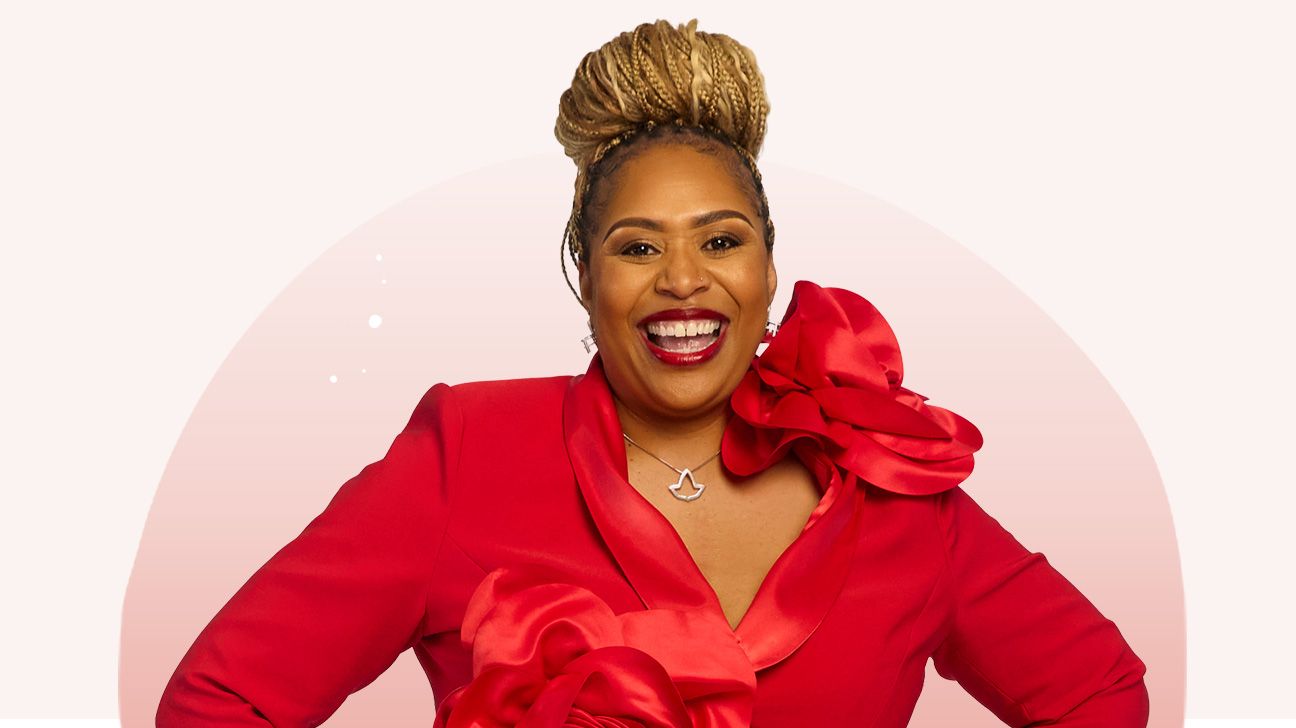 Chanelle, wearing a red dress, smiles with her hands on her hips