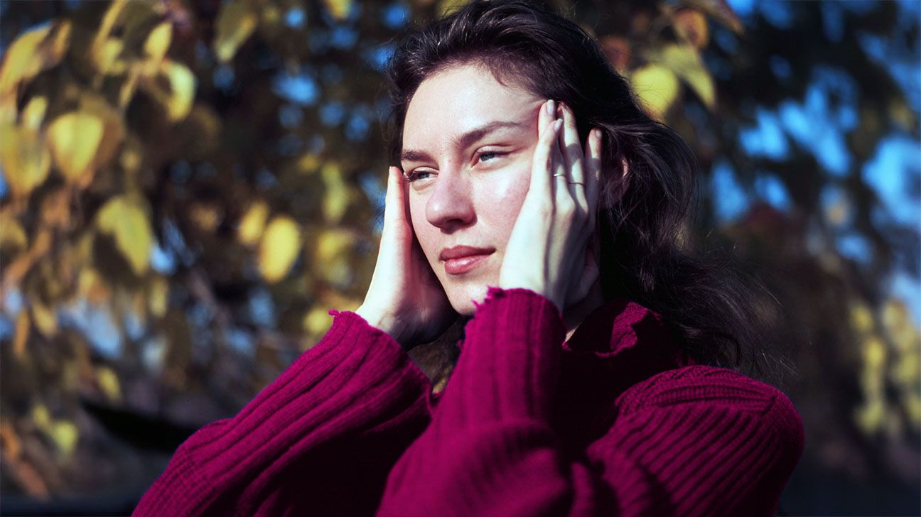 Female standing outside rubbing her temples, as thought stressed