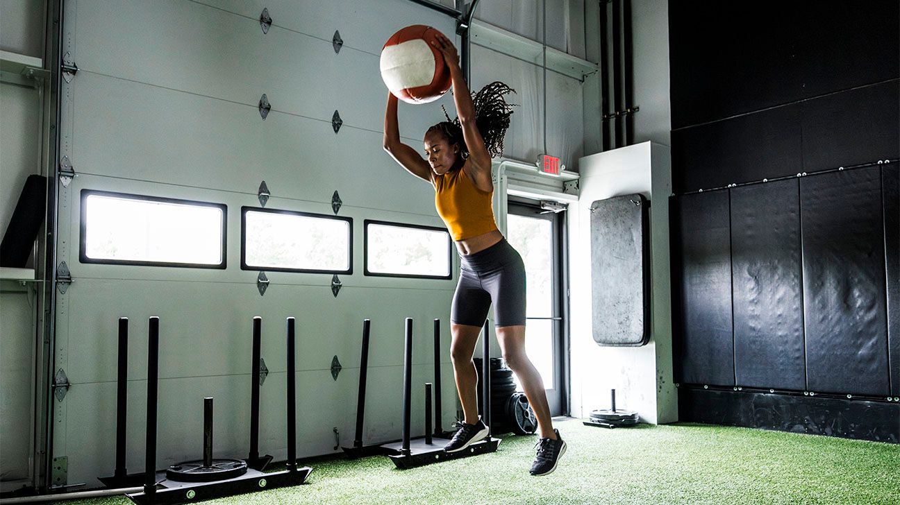 Female jumping up to catch a large ball in a gym setting