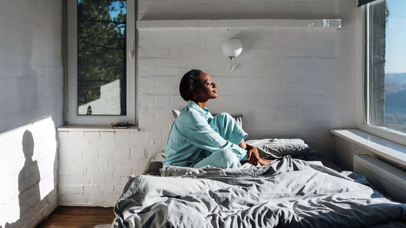 Person sitting on their bed with sun shining on them through the window