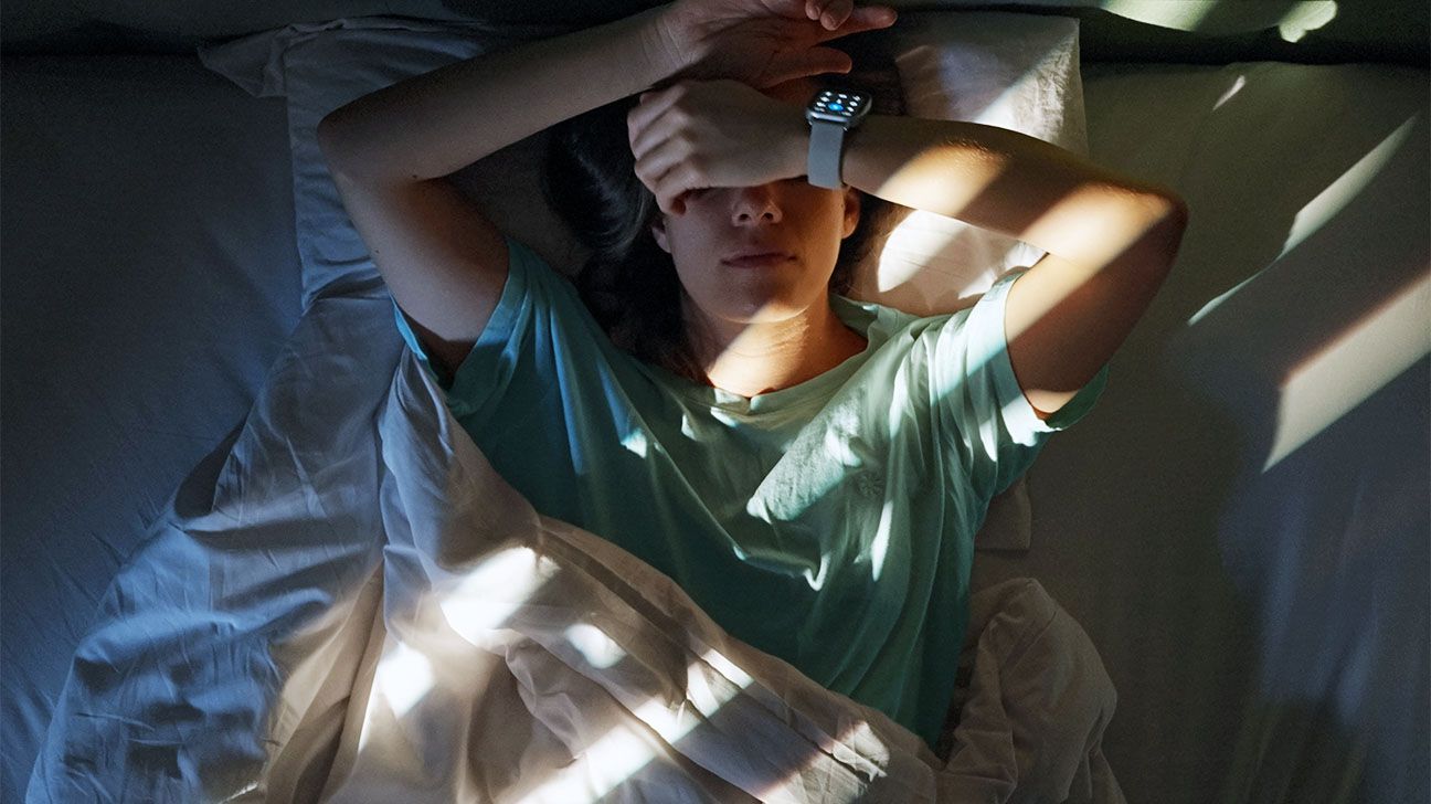 Female wearing smart watch lying in bed with her hands covering her face