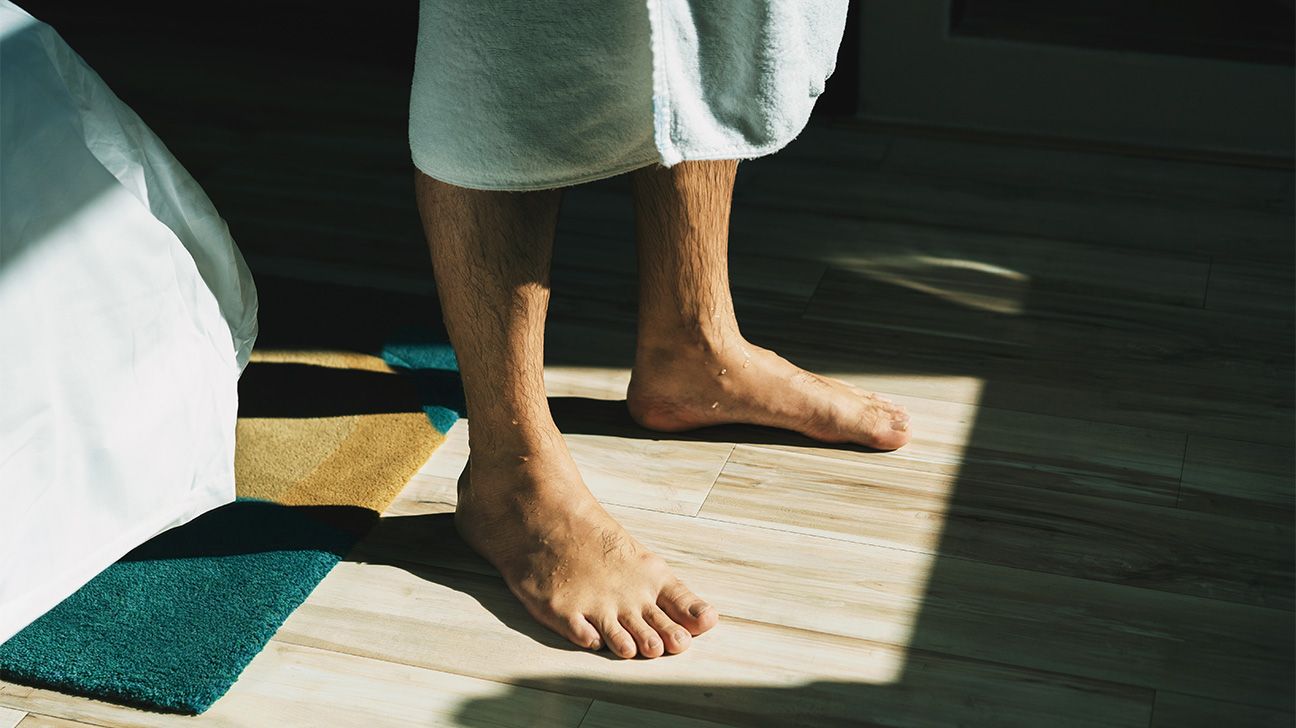A male's bare legs and feet under a towel, standing in sunshine
