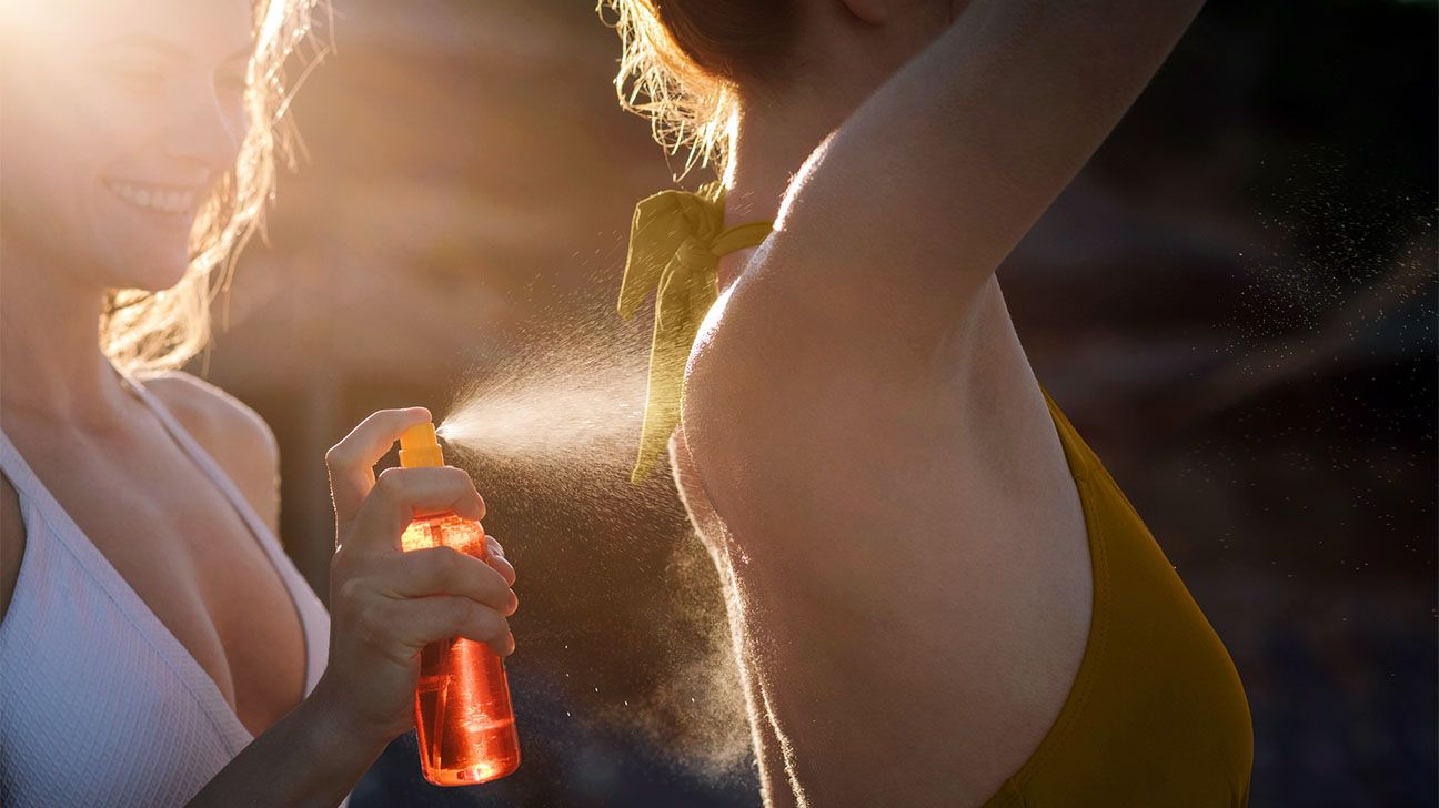 A female spraying sunscreen onto another female while outside in the sun