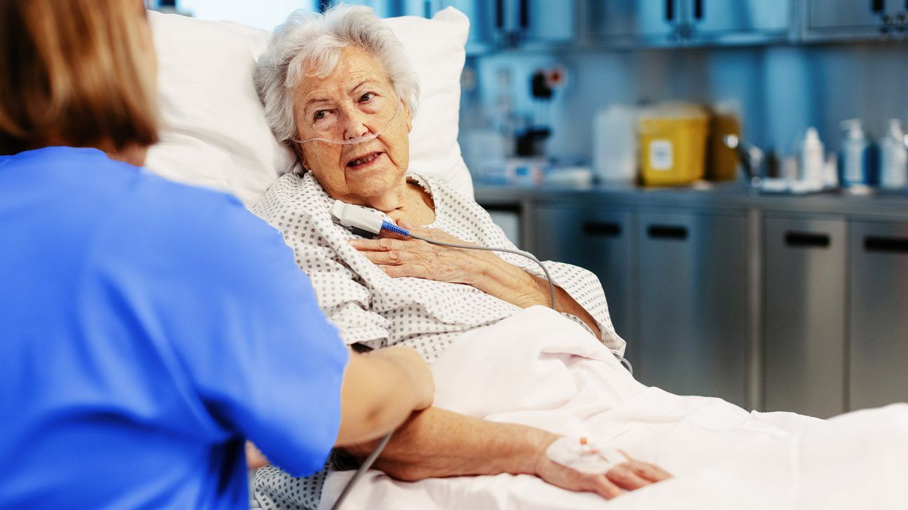 Older female patient in hospital bed talks with doctor