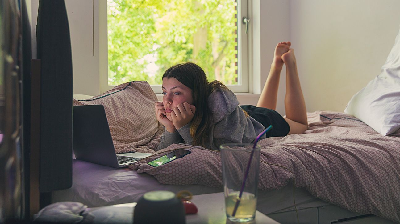Teenaged female lying on her bed looking at a laptop