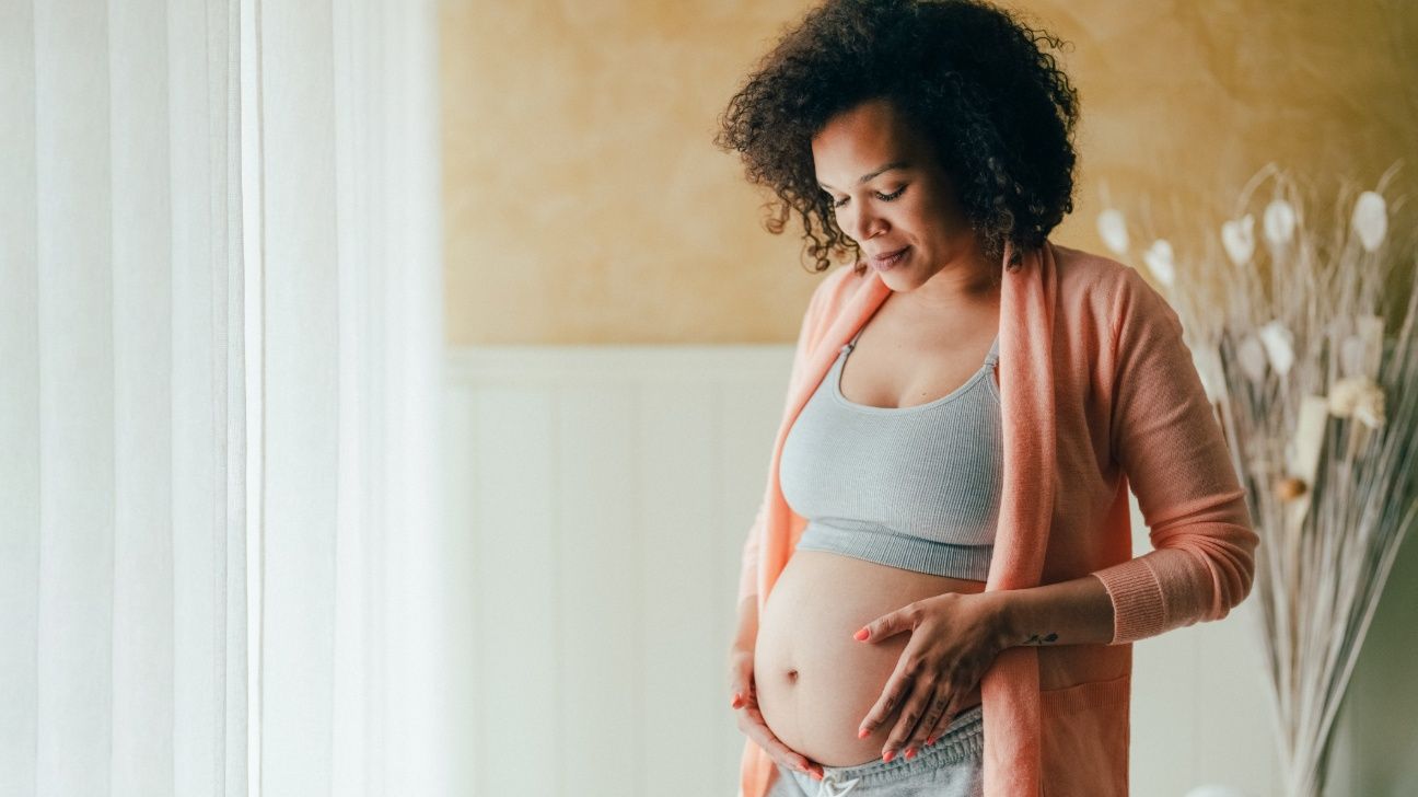 Ethnic pregnant female caressing her belly and looking down at it