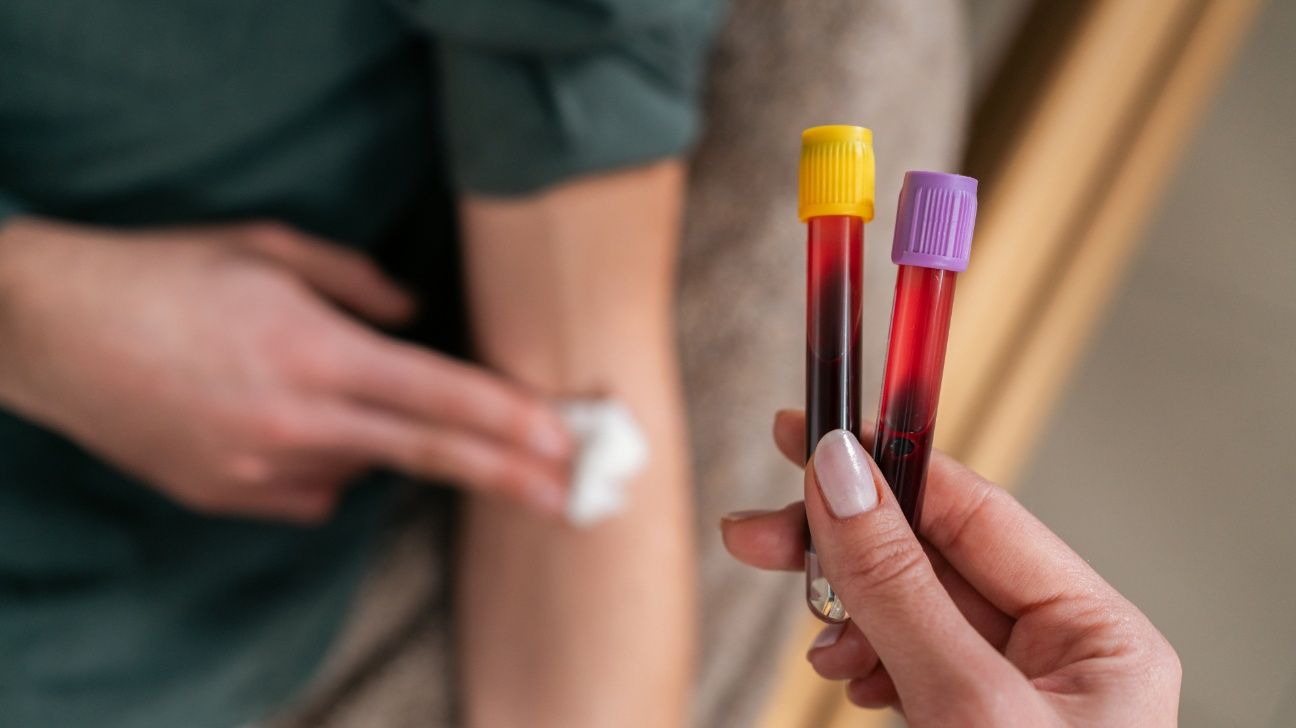 Female holding vials from a blood test in front of patient's arm