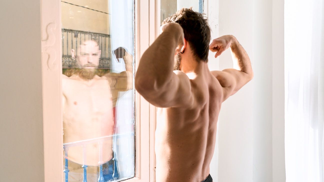 Young male flexes biceps in window reflection