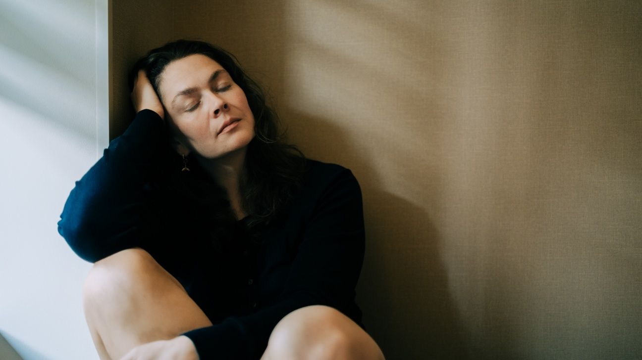 Tired female leans against wall with eyes closed
