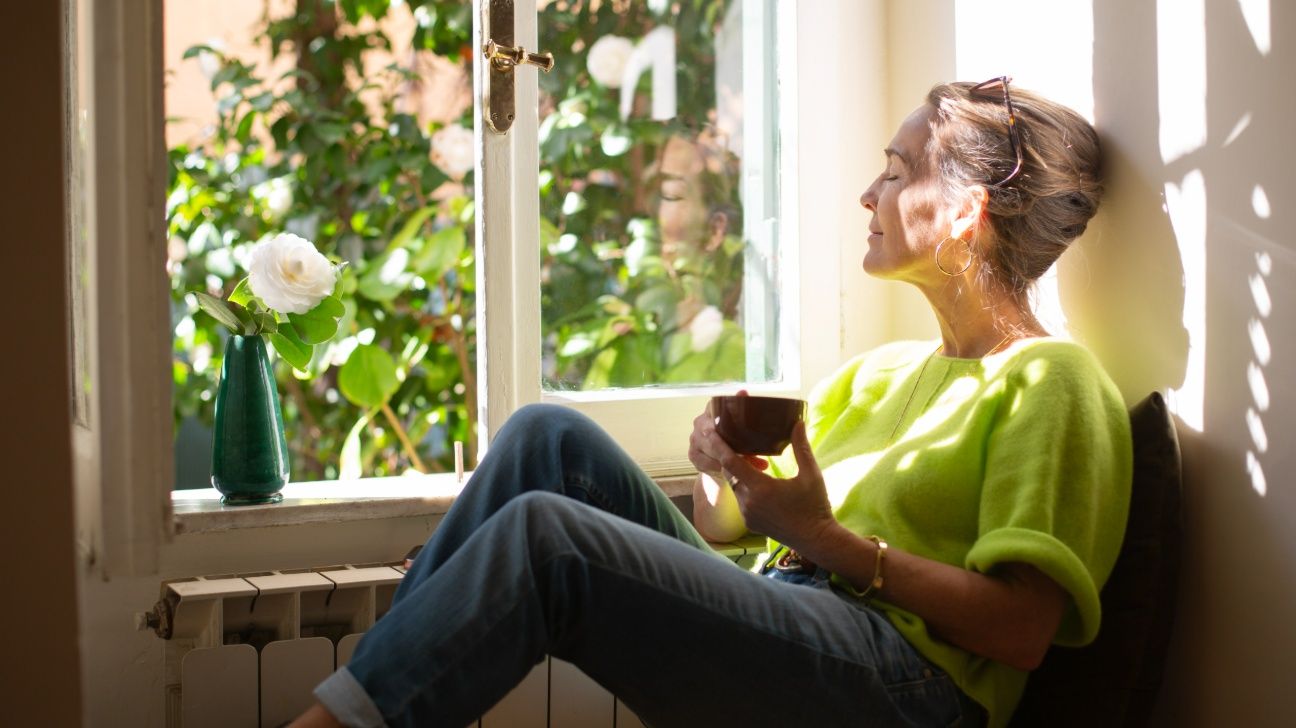 Middle aged female sitting in a window with a cup of coffee