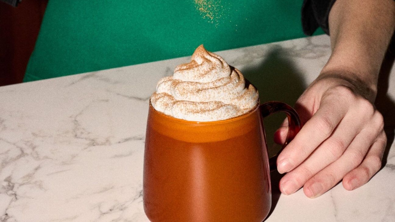 Barista sprinkling pumpkin pie spices on top of a pumpkin spice latte in an orange mug