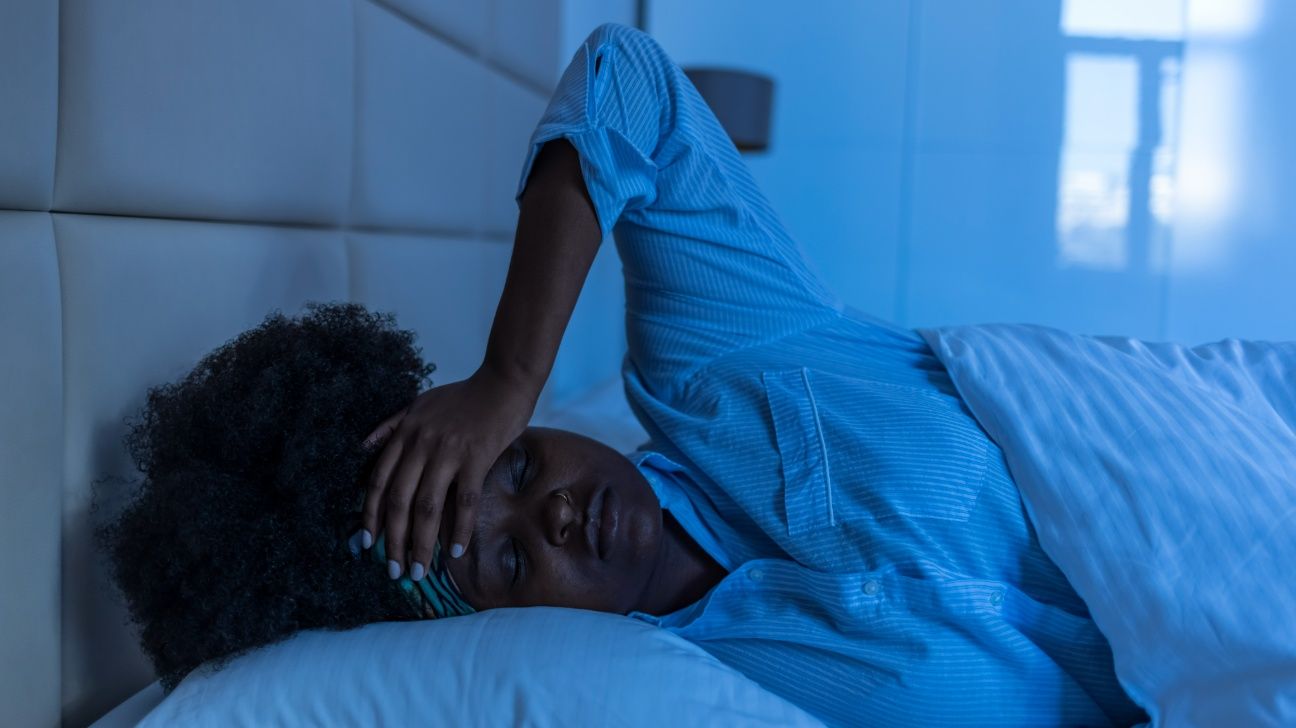 Female lying in bed at night trying with her hand on her head