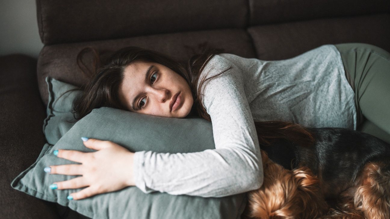 Younger female lying on a sofa with her small dog