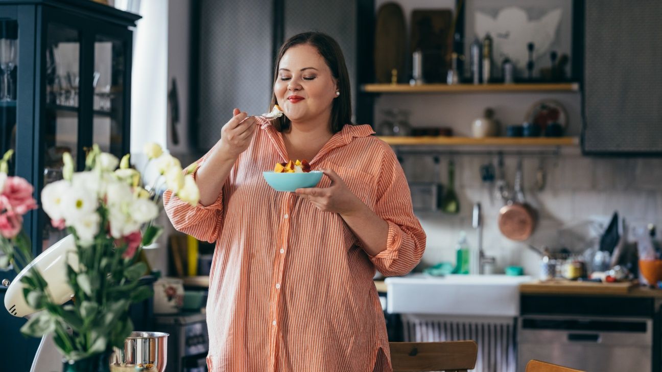 Female standing in a kitchen eating a bowl of fruit salad