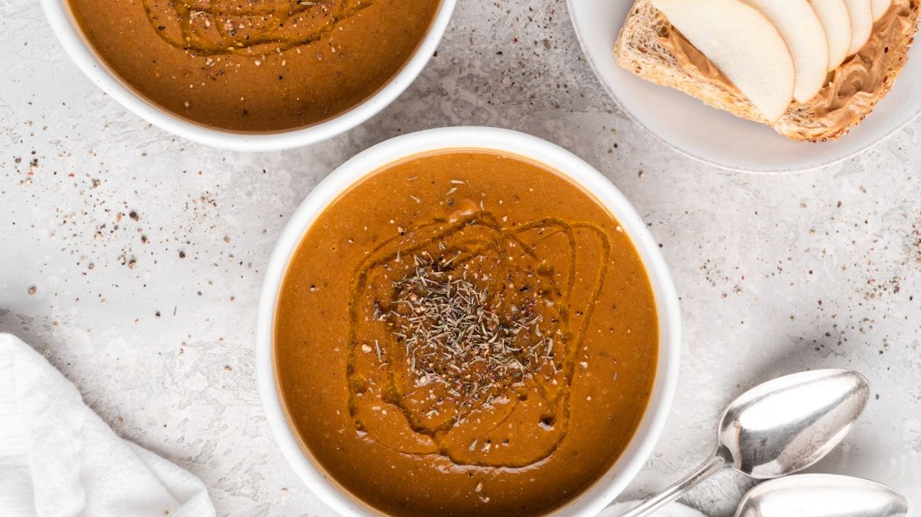 Fennel-apple soup in a white bowl alongside peanut butter and apple slice toast on a white plate