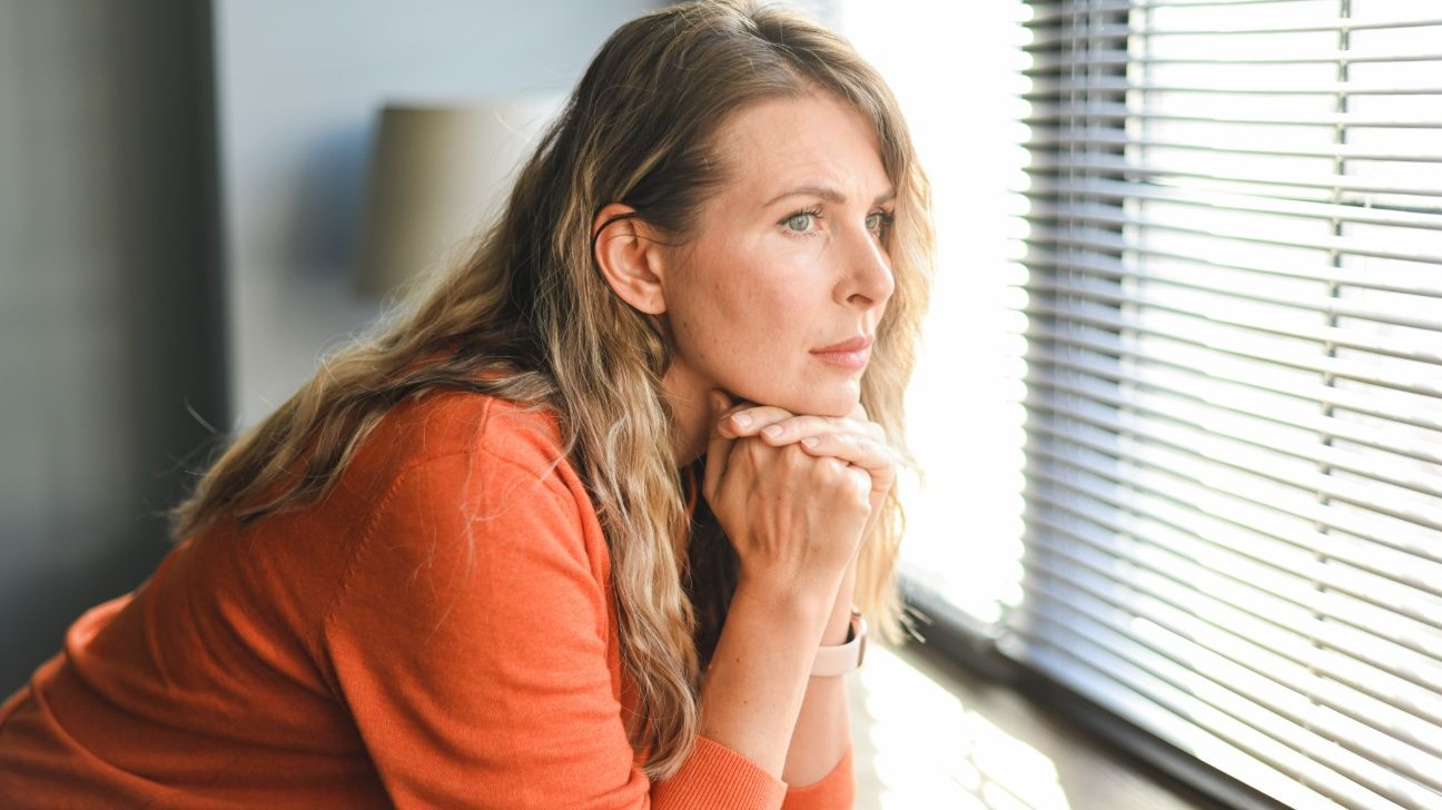 Middle-aged female lost in thought looking out a window