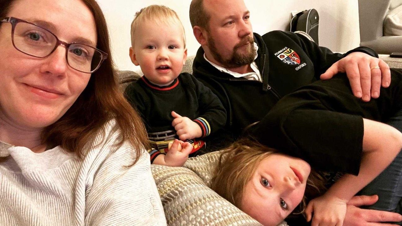 A family of four, parents and two young children, take a selfie on the couch