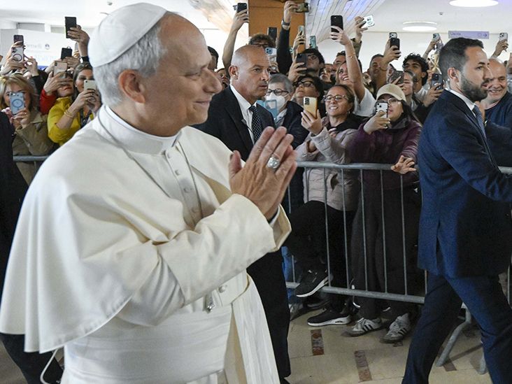 Pope Leo XIV greeting a crowd holding up smartphones behind barriers
