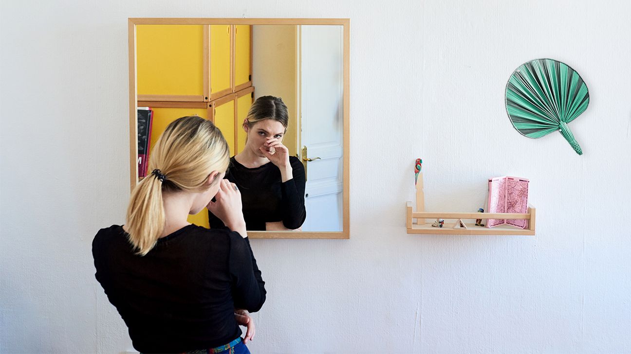 woman looking in the mirror with a hand covering her face