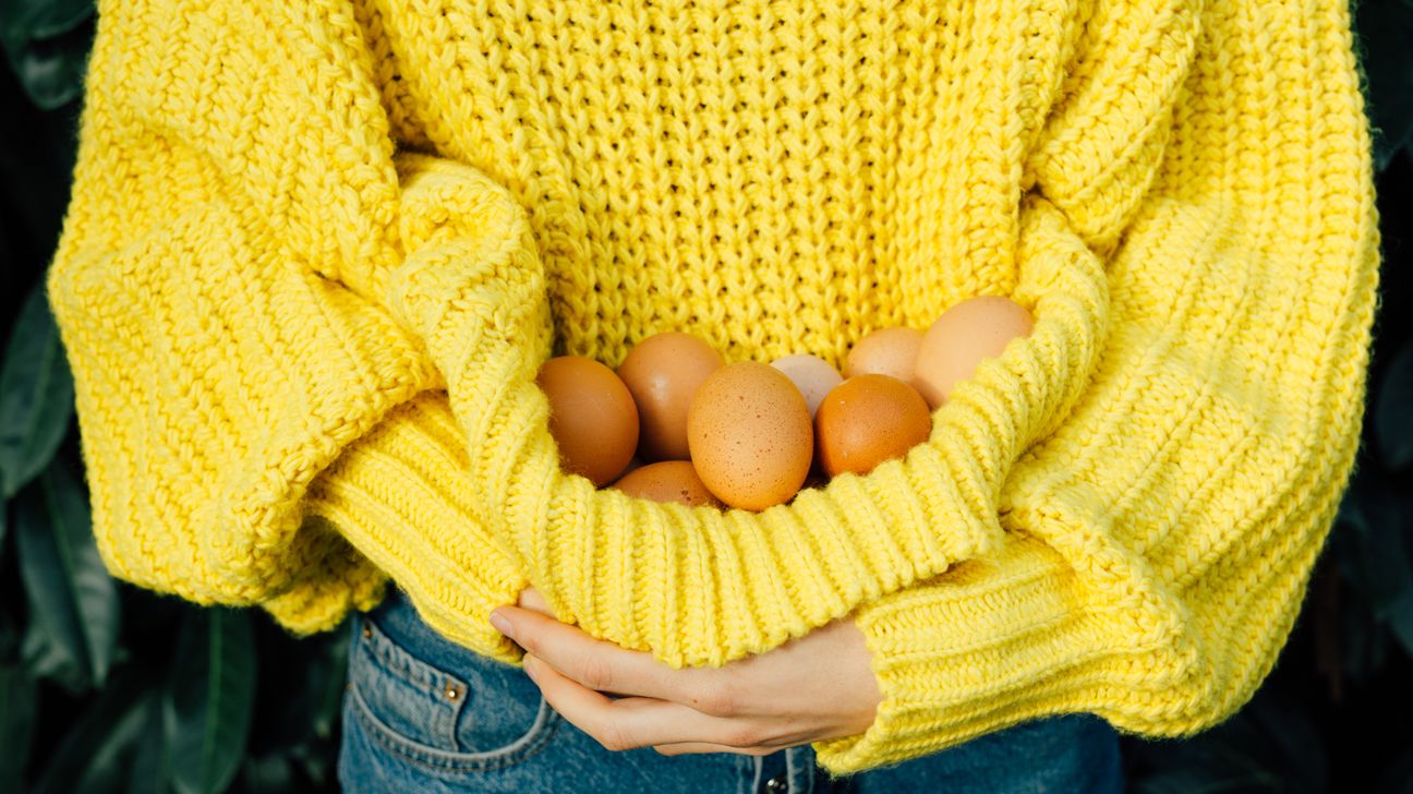 Closeup on a girl holding eggs in her bright yellow sweater