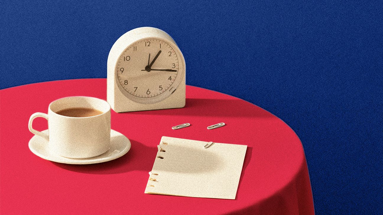 A cup of coffee next to blurred note pad and alarm clock on table, blurred newspaper on table header crop